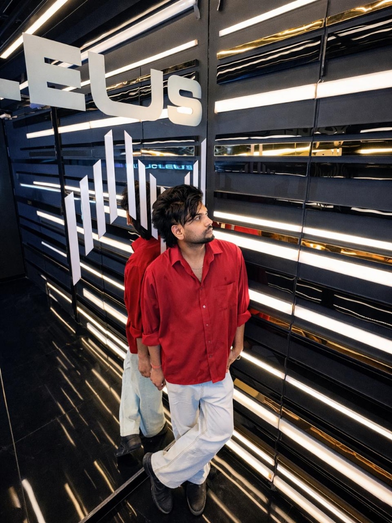 DJ Arush in Red Shirt Leaning against Neon Lights